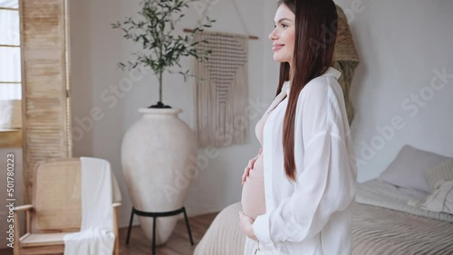 Happy pregnant woman comes to window holding big belly photo