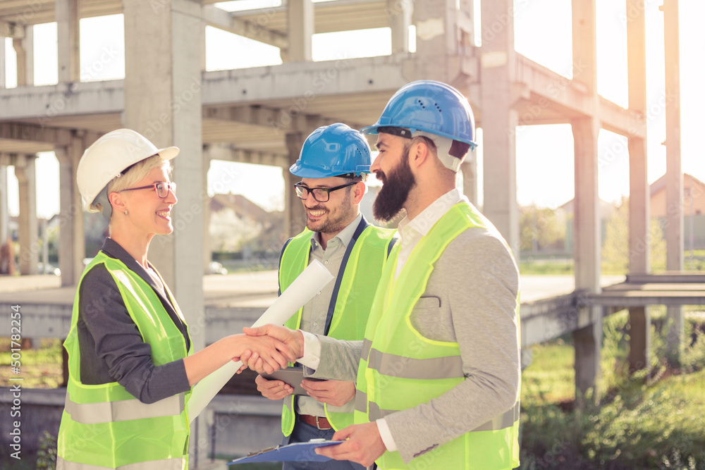 Happy mixed group of young architects talking and shaking hands during meeting on a construction site Happy mixed group of young architects talking and shaking hands during meeting on a construction site