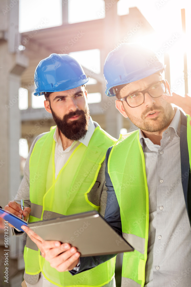 Fototapeta premium Two serious young male engineers or architects discussing and talking on a construction site