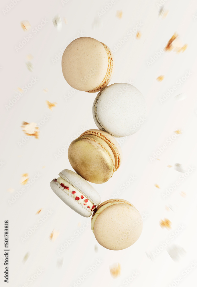 White, yellow, gold macaron cookies. Colorful, sweet small French macaroon cakes. Light beige blurred background with broken macaron cuts, bits, bitten parts. Five cookies in the center of photo