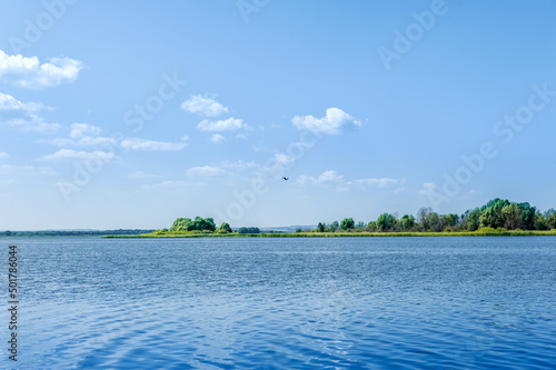 Endless summer landscape. Lake, forest and clear blue sky with beautiful little clouds.