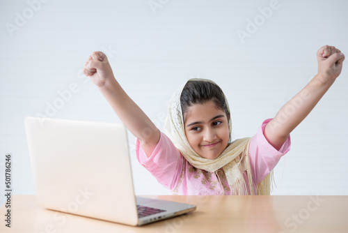 muslim girl using a laptop computer and raised hand for celebrating good news on the table © offsuperphoto
