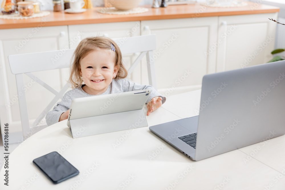 Happy little girl smiling and looking to the camera while watching cartoons. Pretty kid sitting at home while quarantine. The concept of learning at home for schoolchildren Happy little girl smiling and looking to the camera while watching cartoons. Pretty kid sitting at home while quarantine. The concept of learning at home for schoolchildren