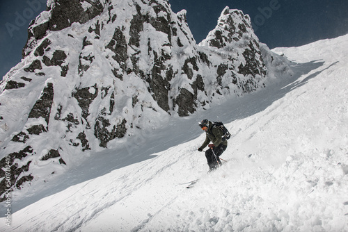 Skier dressed in brown and black sportswear with go-pro camera oh his helmet sliding down snow-covered slopes