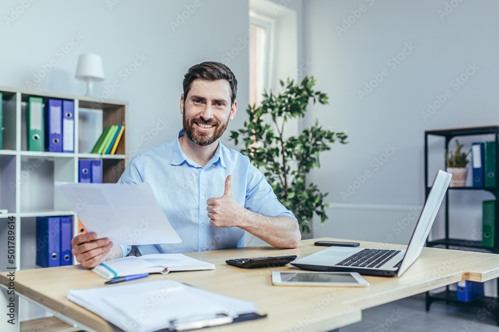 Successful businessman auditor looks at the camera and smiles, performs reconciliation of business reports, shows the camera a thumbs up Successful businessman auditor looks at the camera and smiles, performs reconciliation of business reports, shows the camera a thumbs up