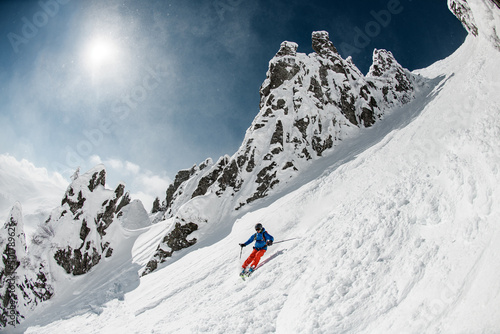 Skier dressed in bright sportswear with fast sliding down snow-covered slopes on skis.