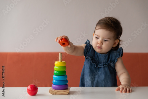 Baby girl playing with wooden colourful toy pyramid at home.