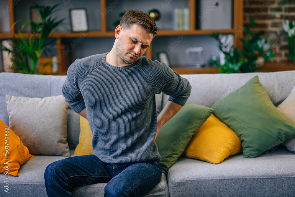 Health care and problem concept - unhappy man suffering from pain in back or reins at home Health care and problem concept - unhappy man suffering from pain in back or reins at home