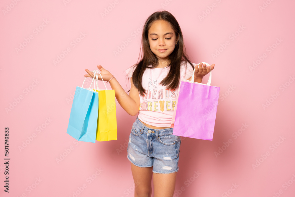 Sale. Cute little girl with many shopping bags on pink background. Portrait of a kid on shopping. Shopping child