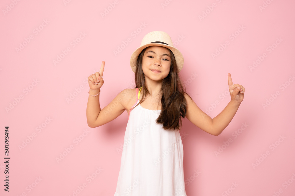 Cheerful little kid girl years old in white dress isolated on pink background children studio portrait. Childhood lifestyle concept. Mock up copy space. Pointing index fingers up Cheerful little kid girl years old in white dress isolated on pink background children studio portrait. Childhood lifestyle concept. Mock up copy space. Pointing index fingers up