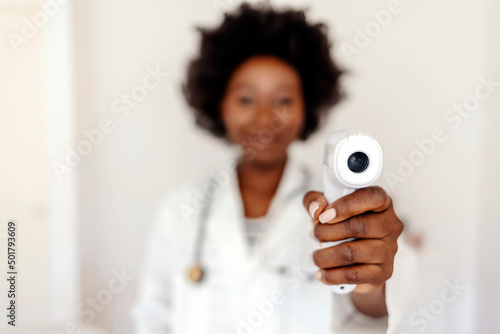 Professional female doctor wearing a white coat, showing digital thermometer isolated on white background. Doctor ready to use infrared forehead thermometer (thermometer gun) to check body temperature photo