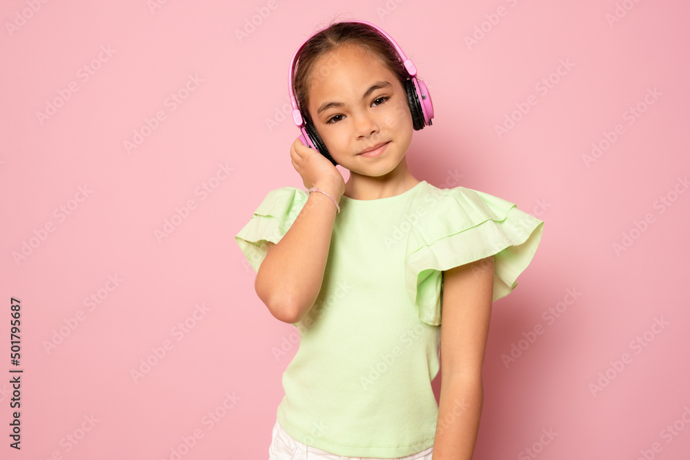 Beautiful cute happy little girl with headphones standing isolated over pink background. Beautiful cute happy little girl with headphones standing isolated over pink background.