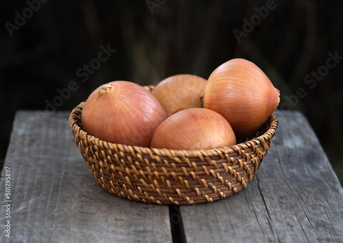 Brown fresh onions in wooden plate on black background.