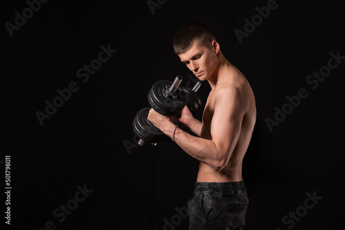 young handsome muscular man doing exercises with dumbbells on a black background