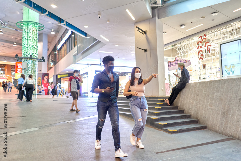 Asian woman wearing mask pointing ahead while walking with a friend in a mall