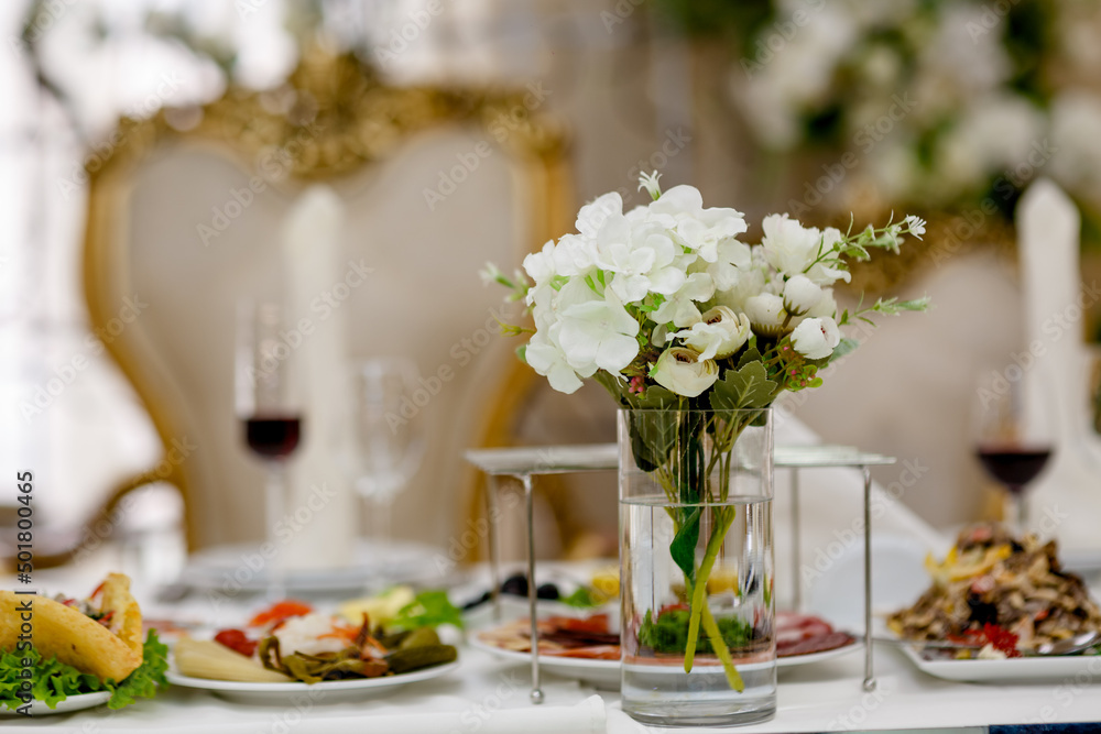 Classic and elegant artificial white decorative roses in glass full of water on wedding presidium