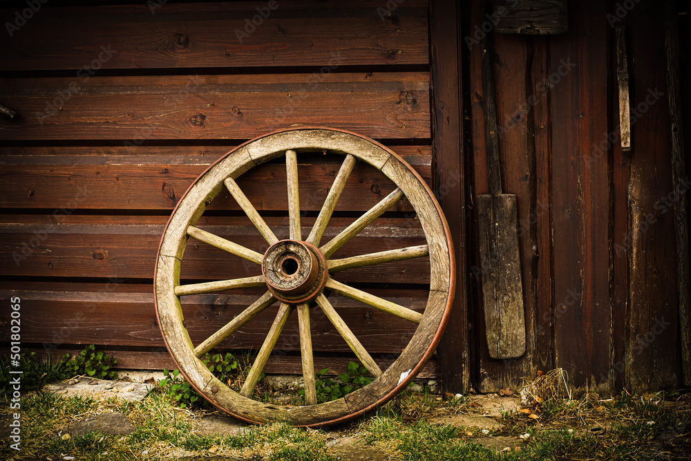 Old rusty wagon wheel leans against barn.Peasant tool.