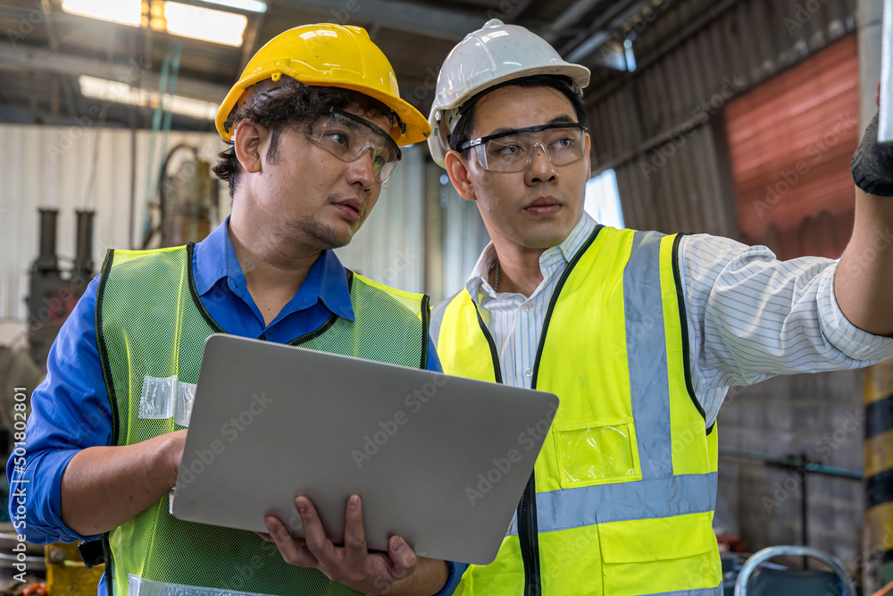 Foreman or Professional technician holding a laptop computer in an industrial factory. Male engineer apprentice trainee with machine in industrial machinery. Foreman or Professional technician holding a laptop computer in an industrial factory. Male engineer apprentice trainee with machine in industrial machinery.