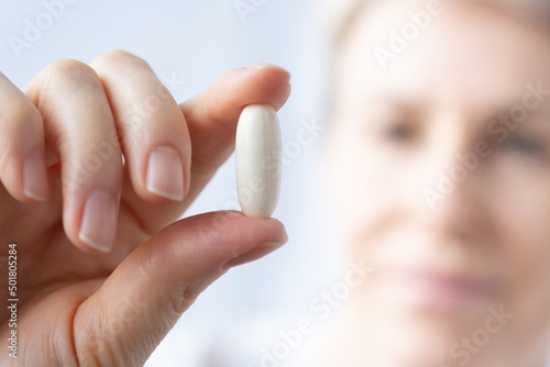 A woman holds a large white pill in her hand and examines it carefully. The hand with the pill is in the foreground in focus