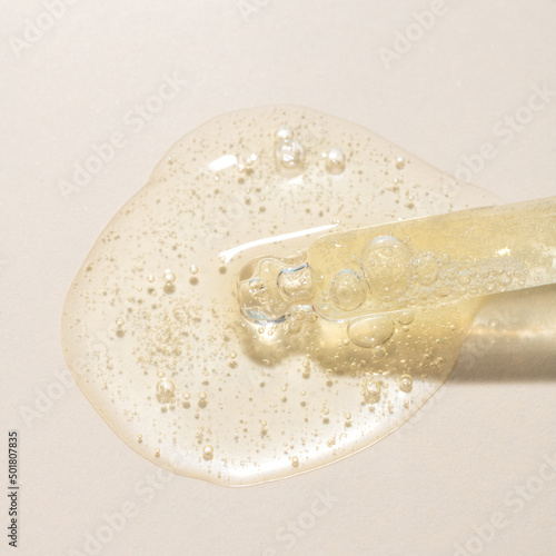 Top view of transparent pipette dropper with light golden drop of serum cosmetics, oil, gel ou cream on beige  background and bubbles of air. Minimal beauty concept, macro closeup with copy space