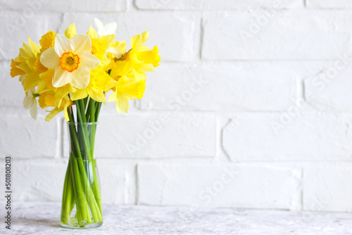 Bouquet of yellow daffodils in a vase against a brick wall. Flower arrangement. Greeting card for the holidays. Minimalism