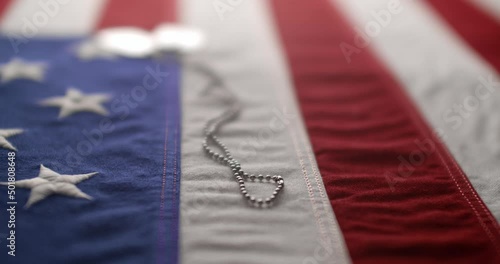 Slow motion of a US American flag with shiny military dog tags. Background for Armed Forces Day, Memorial Day, Veteran's Day, 4th of July, or other patriotic USA holiday.