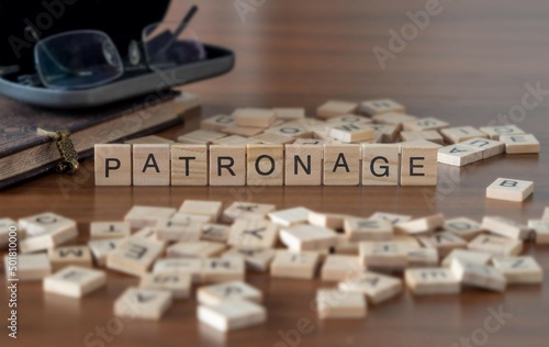patronage word or concept represented by wooden letter tiles on a wooden table with glasses and a book