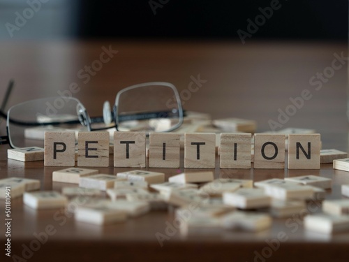petition word or concept represented by wooden letter tiles on a wooden table with glasses and a book photo