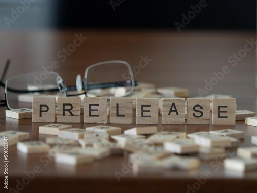 prelease word or concept represented by wooden letter tiles on a wooden table with glasses and a book photo