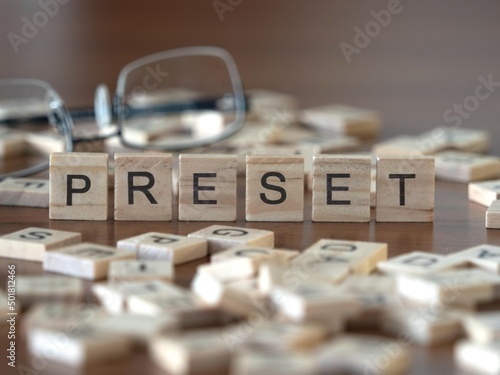 preset word or concept represented by wooden letter tiles on a wooden table with glasses and a book photo