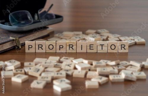 proprietor word or concept represented by wooden letter tiles on a wooden table with glasses and a book photo