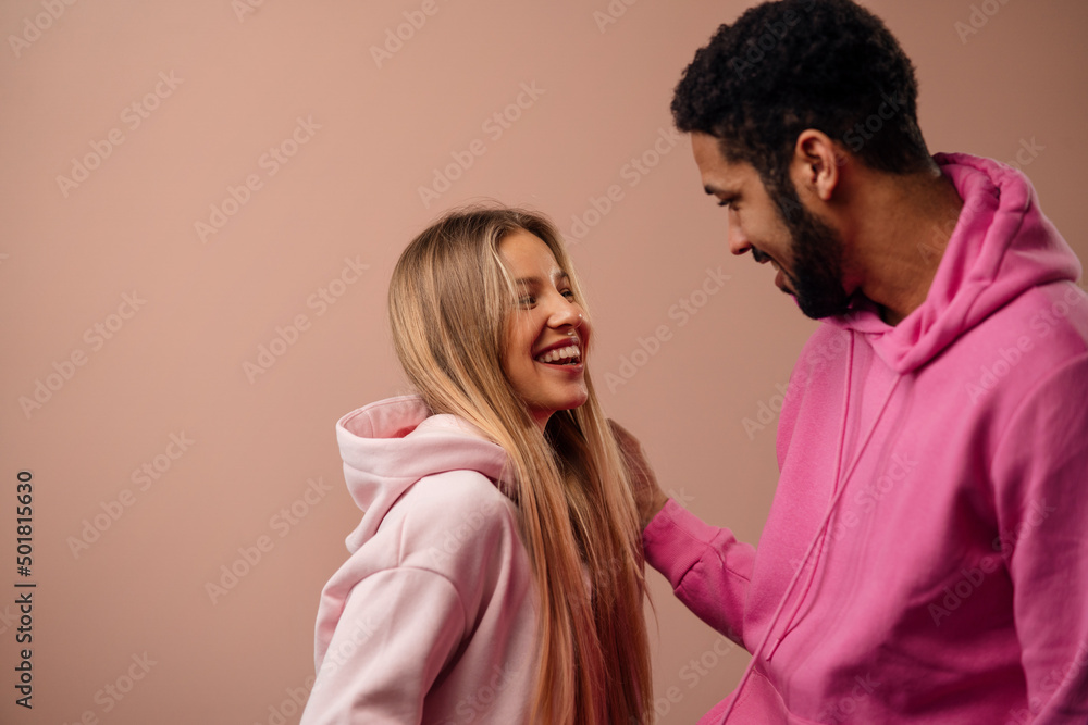 Fashion studio portrait of a happy young couple in hoodie posing over pink background. Fashion studio portrait of a happy young couple in hoodie posing over pink background.