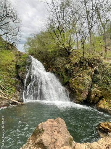 forest in spring with a large waterfall pouring its water into a pond  rocks in the foreground  Xorroxin water fall  Erratzu  Navarra  Spain