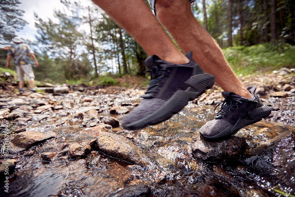 Close-up of man's legs while crossing a creek during a hiking. Hiking, nature, relationship, together Close-up of man's legs while crossing a creek during a hiking. Hiking, nature, relationship, together