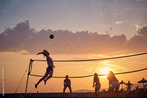 Friends playing volleyball on beach at sunset photo