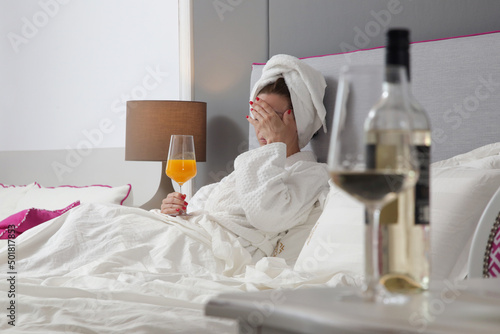 Young woman waking up with hangover and headache, drinking fresh squeezed orange juice to feel better 