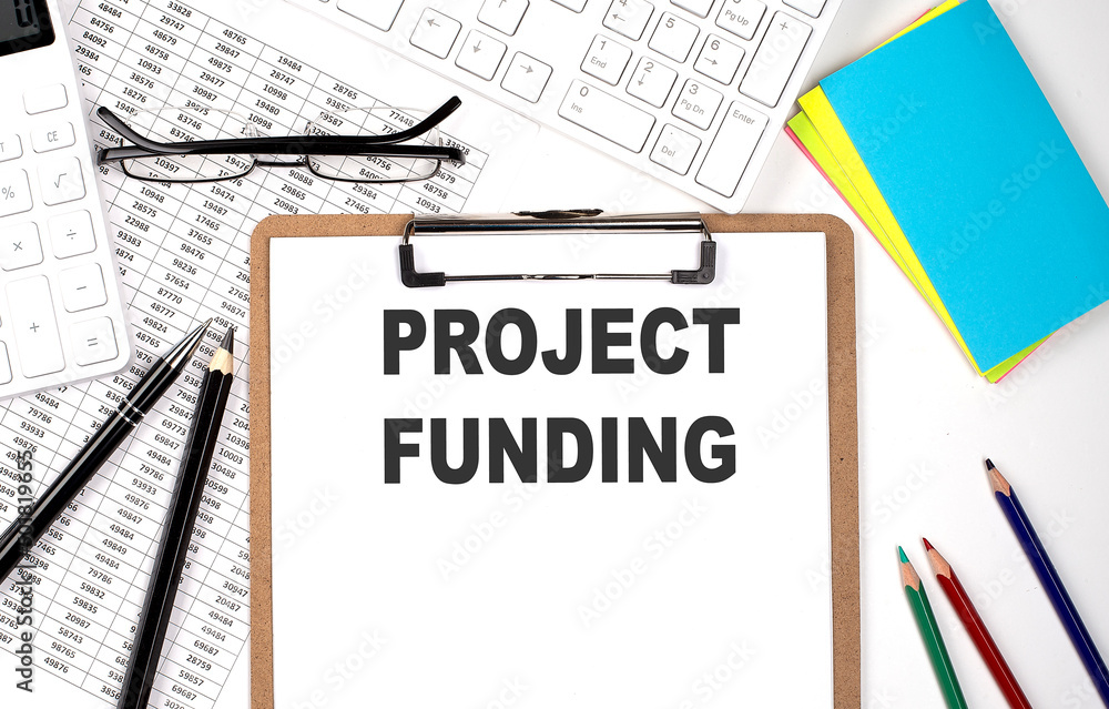 Clipboard with text PROJECT FUNDING and keyboard and chart on the white background. Clipboard with text PROJECT FUNDING and keyboard and chart on the white background.