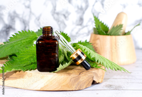 Fresh nettle in wooden mortar. Preparation of elixirs from medicinal herbs by herbalists. The essential oil in the pharmacy bottle with pipette at cosmetologi photo