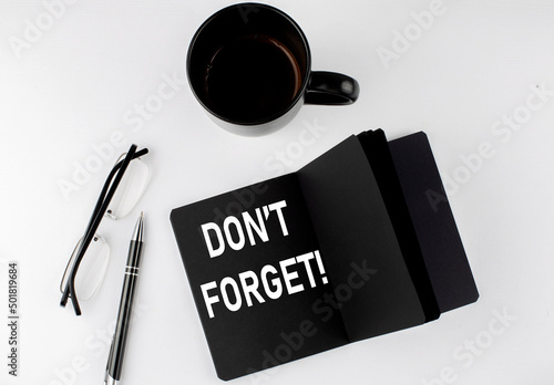DON'T FORGET written text in small black notebook with coffee , pen and glasess on white background. Black-white style
