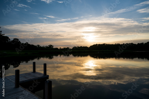 the sun sets over a pier and a lake one summer evening
