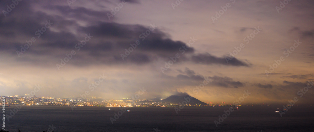 Dramatic clouds over coastal city and hill at night