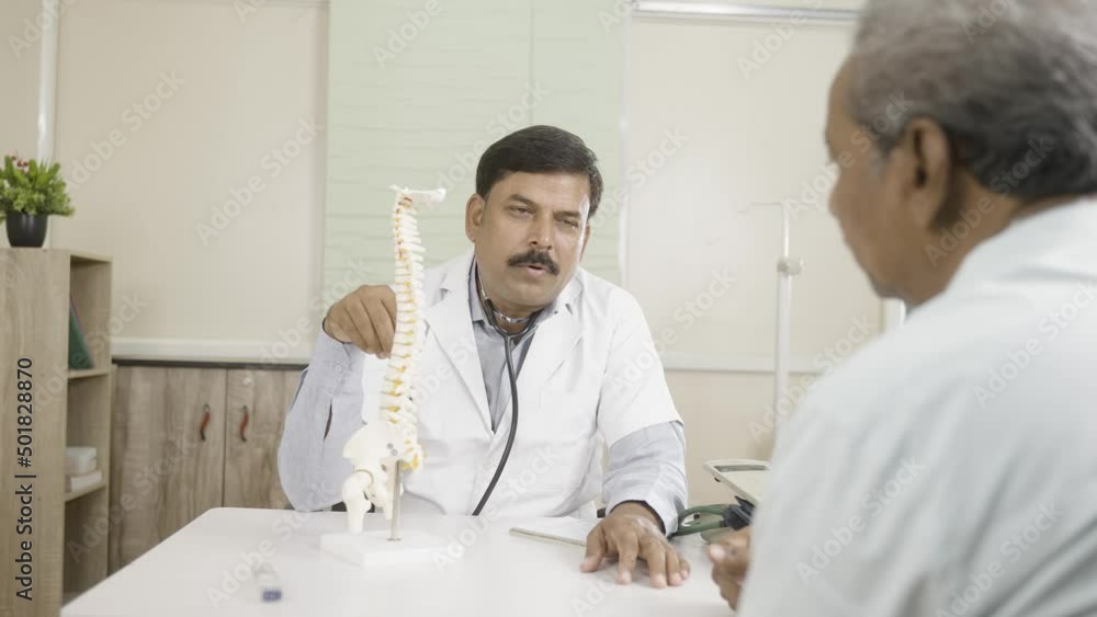 Shoulder shot of doctor explaining to senior patient abour back pain using spinal model at hospital - concept of consultation and counseling Shoulder shot of doctor explaining to senior patient abour back pain using spinal model at hospital - concept of consultation and counseling