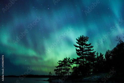 Tablou canvas Northern lights erupt over a lake in Minnesota in a dark sky overhead shining ra