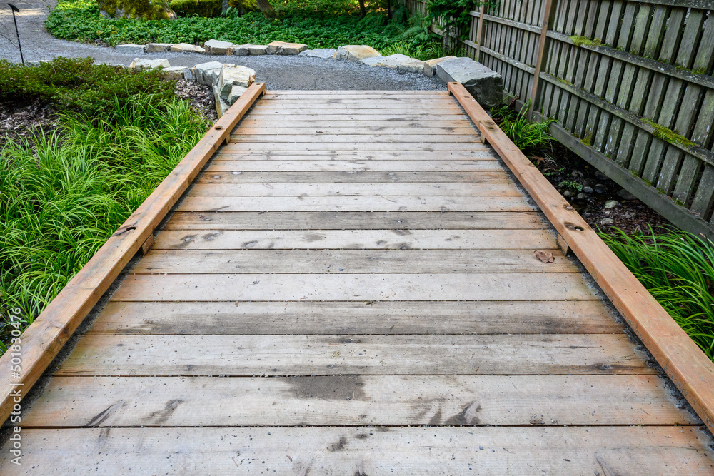 Obraz premium Wooden boardwalk, an invitation to explore a woodland garden 