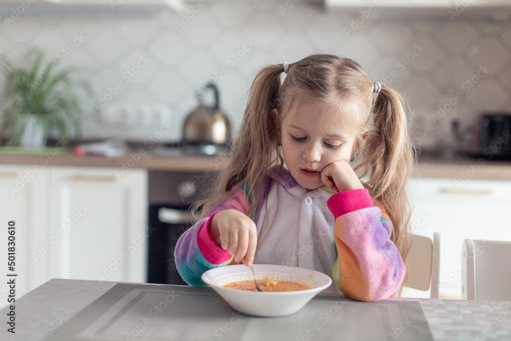 cute little girl eats soup at home in the kitchen without appetite. The child sadly looks at the plate, does not want to eat. Healthy food, natural vitamins, baby food concept. selective focus cute little girl eats soup at home in the kitchen without appetite. The child sadly looks at the plate, does not want to eat. Healthy food, natural vitamins, baby food concept. selective focus
