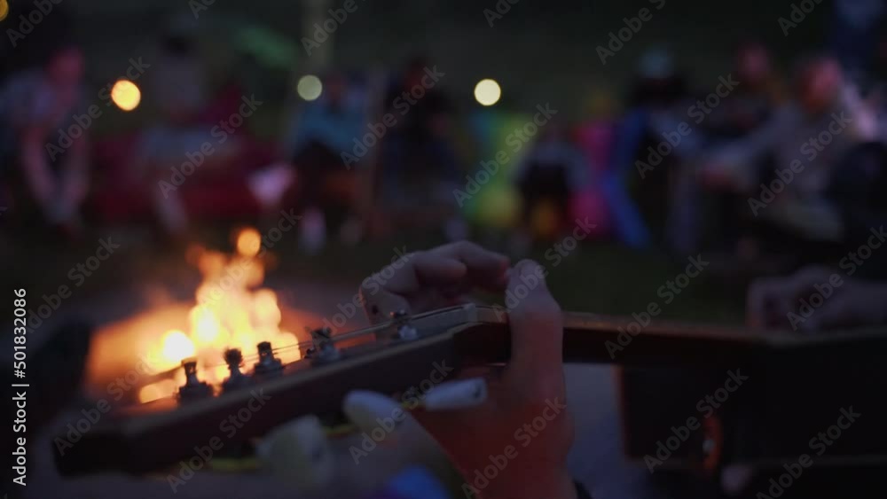 Male hand playing music on guitar on background burning fire flame in night darkness close up. Male hand playing music on guitar on background burning fire flame in night darkness close up.