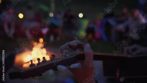 Male hand playing music on guitar on background burning fire flame in night darkness close up. 