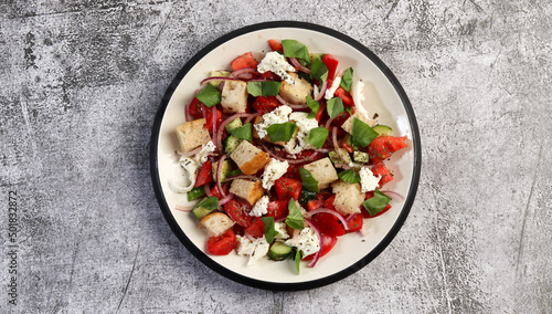 Tuscan Panzanella, traditional Italian salad with tomatoes and bread. Vegetarian panzanella salad on a round plate on a dark gray background. Top view, flat lay