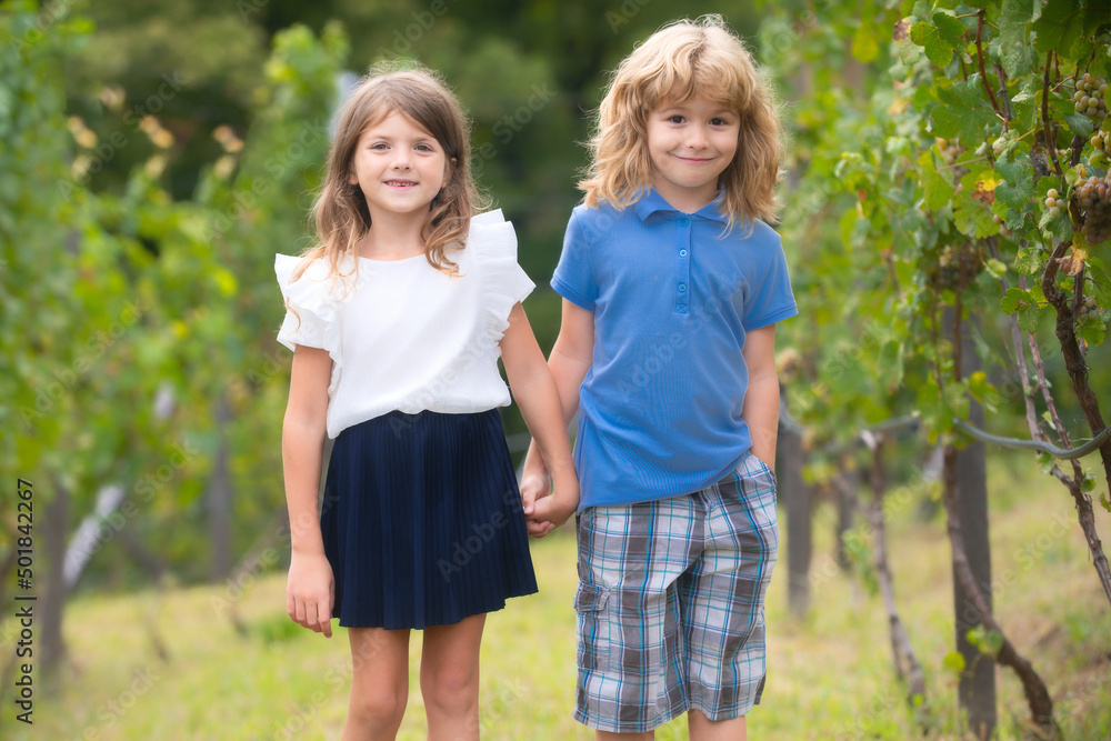 Fototapeta premium Cute little children walking outdoors. Portrait of two happy young kids at the spring park. Cute lovely boy and girl in backyard. Sister and brother walking in garden.