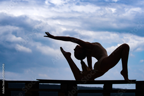 Silhouette of young fit woman stretching. Sporty young girl doing fitness exercise, healthy life. Cloudy sky background.